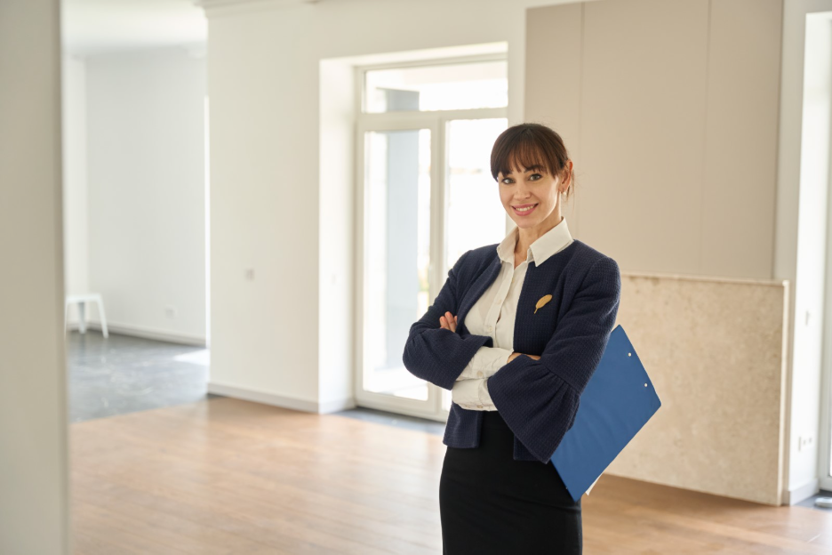Businesswoman holding a blue folder and standing in a bright, newly renovated commercial space with wood flooring and an open layout.